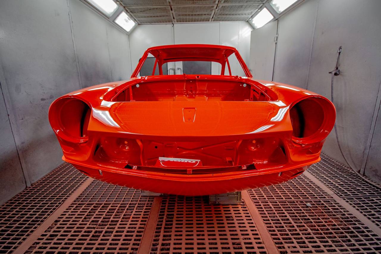 A car body panel freshly painted red inside a spray booth