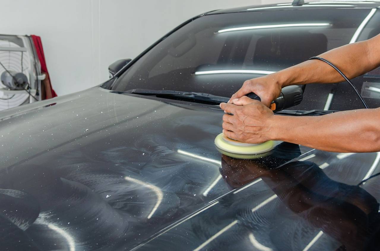 A technician polishing a finished car with a machine buffer