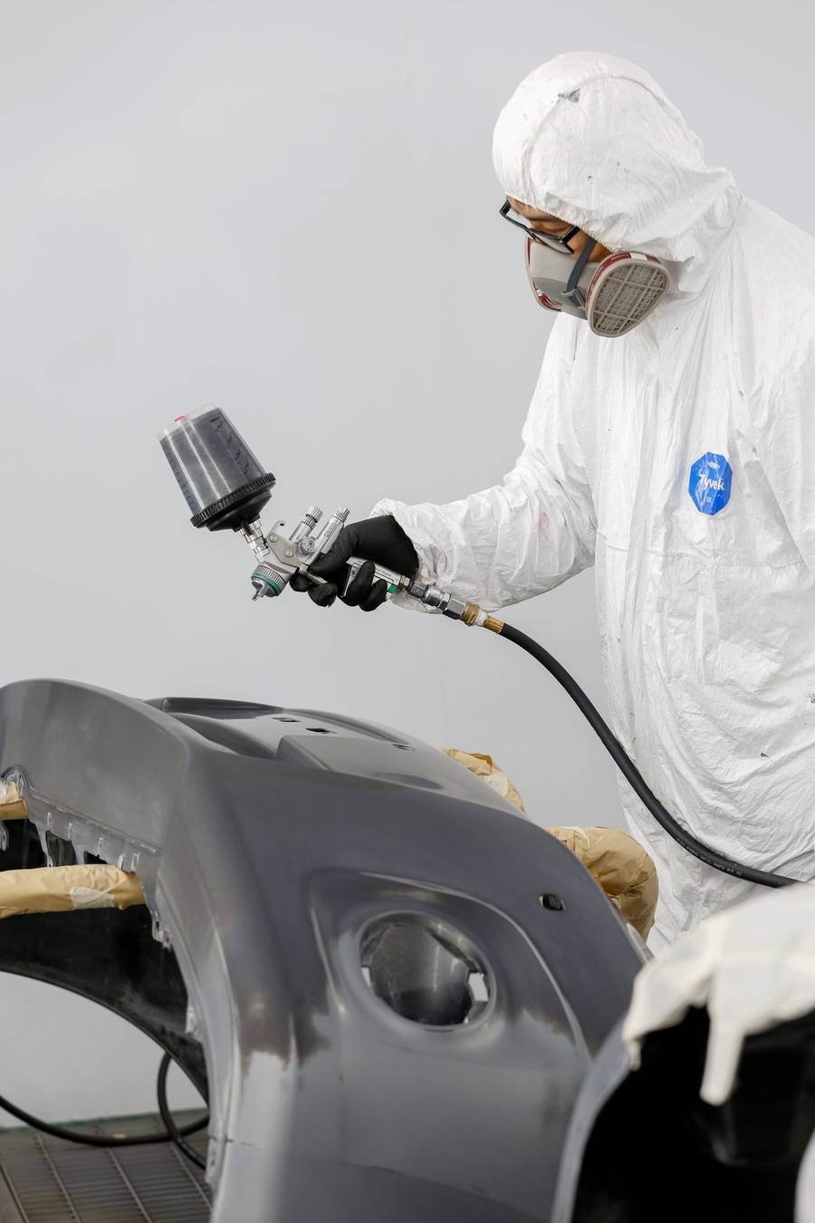 A painter in protective gear spraying a car panel
