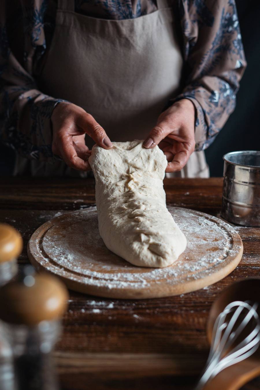 A baker’s floured hands shaping dough on a wooden bench
