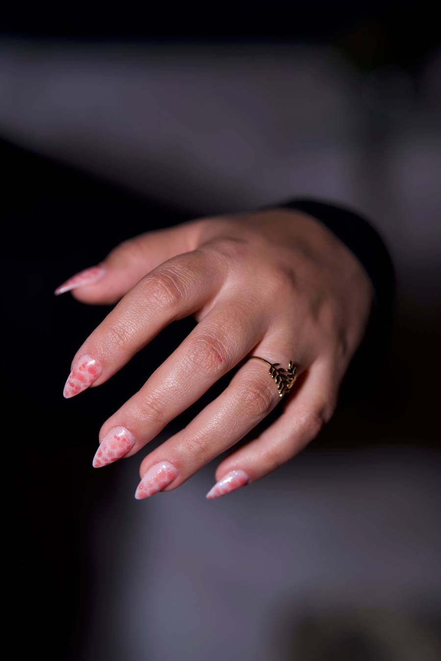 Close-up of a hand with glossy, almond-shaped pink nails against a dark background